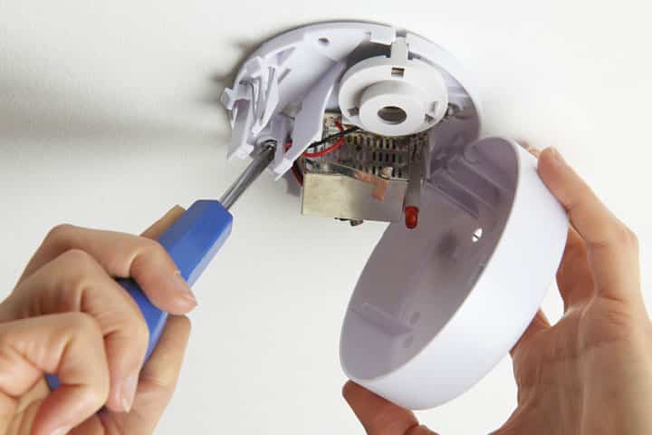 Smoke alarm cover removed and its base being unscrewed from the ceiling