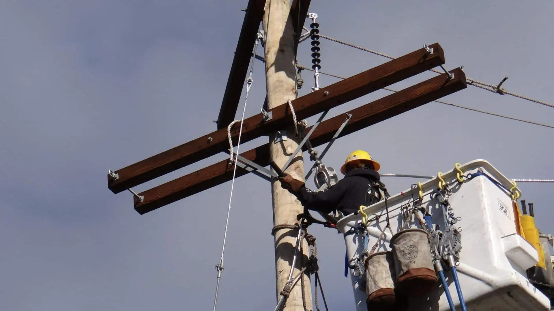 Line worker in a cherry picker beside new crossarms on a timber power pole