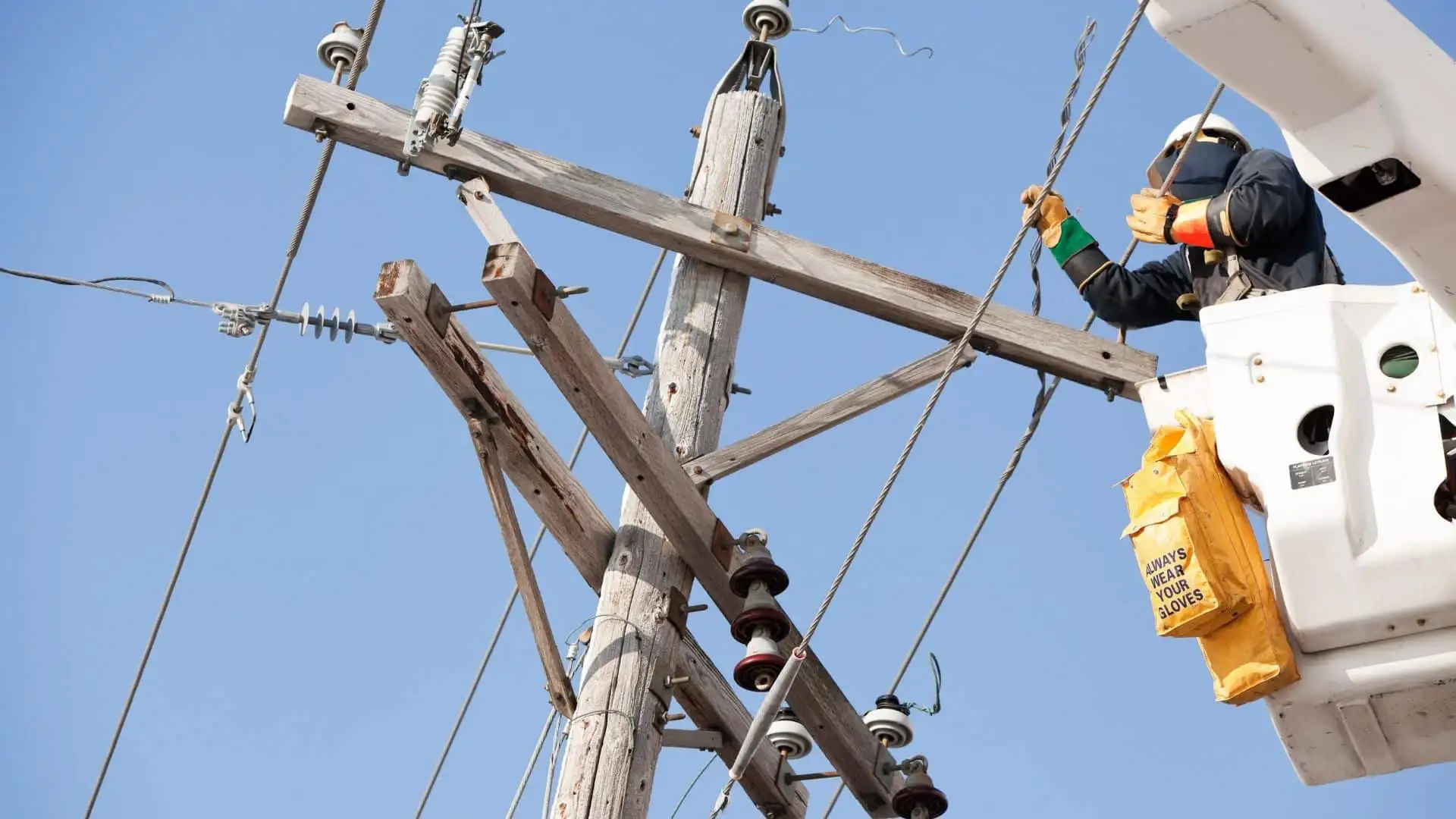 Line worker in an elevated bucket working on a timber power pole