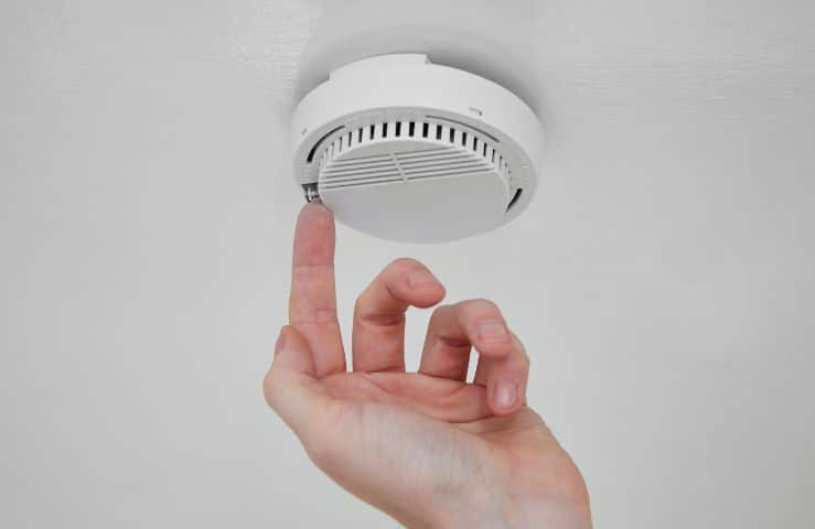Finger pressing the test button on a ceiling smoke alarm
